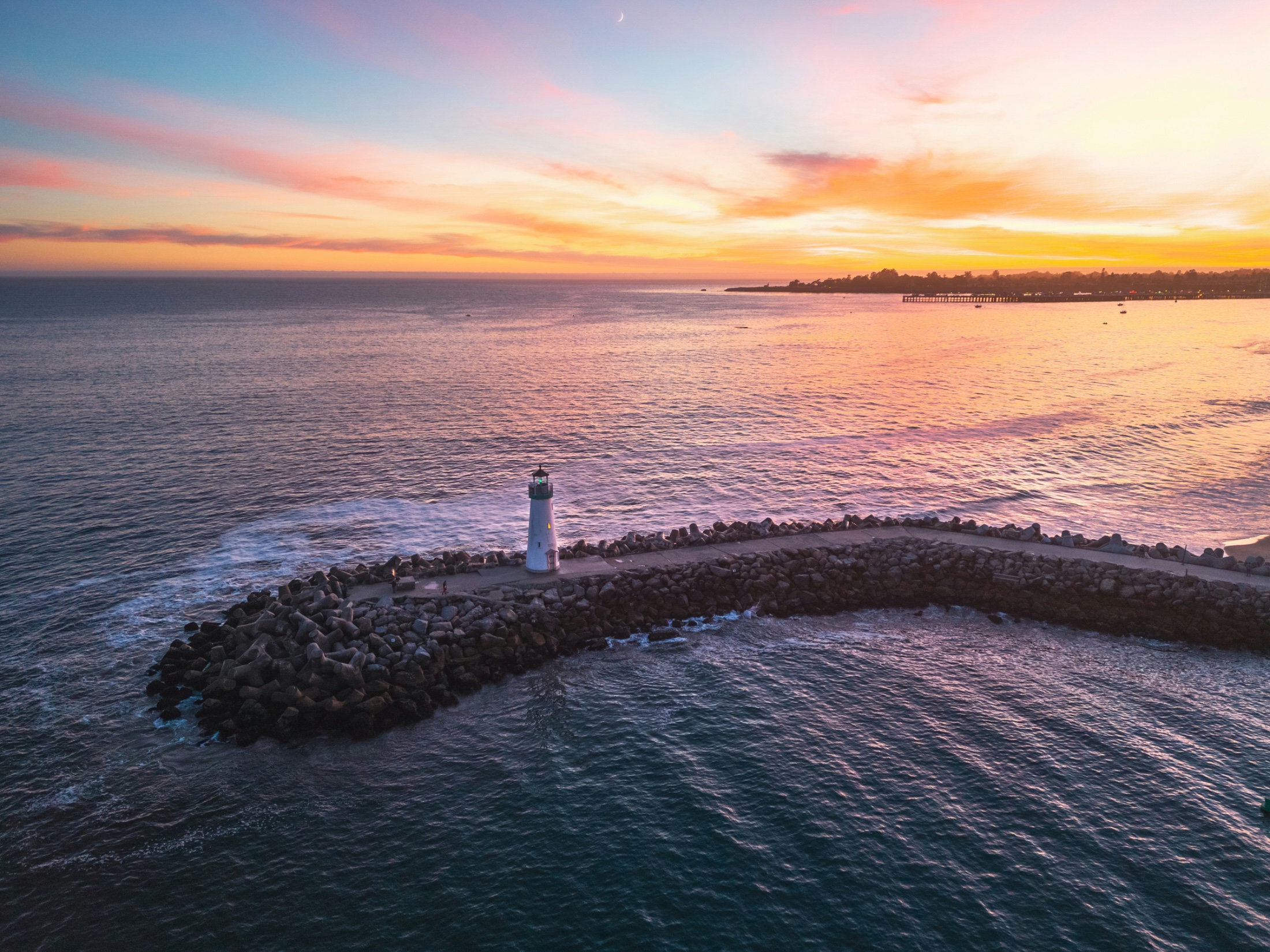 A lighthouse standing at the end of a stone jetty at dusk